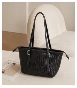 Detail view of black woven leather tote bag featuring slim buckled double straps.