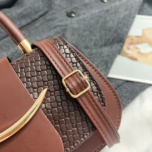 Brown woven leather crossbody bag with metal buckle and curved hardware detail.