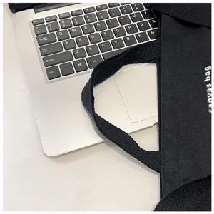 Detail shot of black canvas tote bag showing texture and strap on desk near laptop setup.