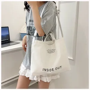 Detail view of large capacity white canvas tote bag with shoulder strap and letter print.
