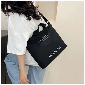 Close-up detail shot of the black canvas tote bag showing the printed text design and strap.