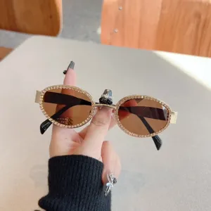 Detailaufnahme trendiger ovaler Strass-Sonnenbrille mit braunen Gläsern und Goldrahmen.