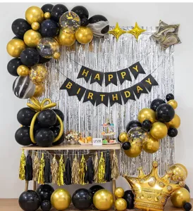 Birthday party decoration scene detail with black gold balloons and silver fringe curtain backdrop.