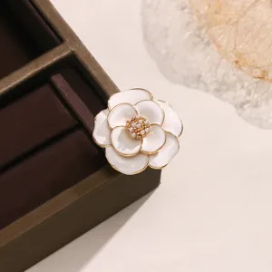 Primo piano di una spilla a camelia bianca come copribottone con bordo dorato e perla.