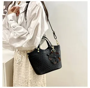 Detail view of a black woven bucket bag with flower charm, worn by model for style reference.