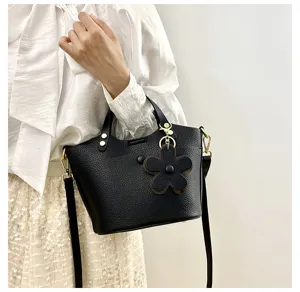 Classic black textured bucket bag for women, stylish leather crossbody handbag with flower charm.