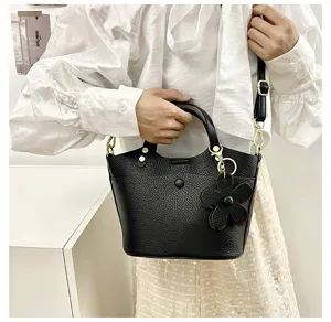 Black faux leather bucket bag with floral charm, stylish detail view of shoulder handbag.