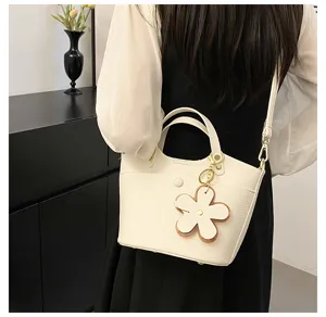 Detailed view of white leather bucket bag with cute flower charm, showing fine texture.