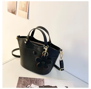 Detailed view of black leather bucket bag featuring elegant flower charm and metal hardware.