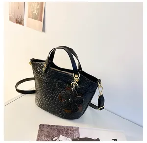 Black woven texture bucket handbag detail showing dual top handles, shoulder strap and flower charm.