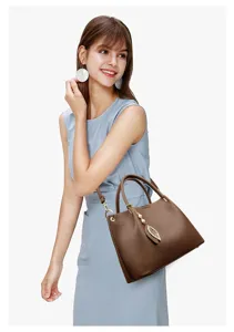 Stylish brown leather tote bag with elegant leaf pendant, shown worn on shoulder by model.