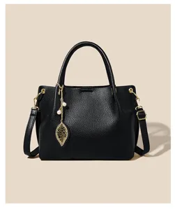Black soft leather handbag detail view, featuring gold hardware and elegant leaf pearl pendant.