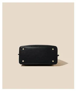 Detail view of women's black leather handbag bottom with four metal feet, minimalist design.