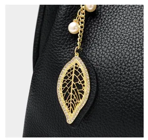 Detailed view of women soft leather handbag with gold rhinestone leaf pendant accessory.