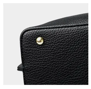 Close-up detail of women's black leather handbag showing textured PU and gold stud.