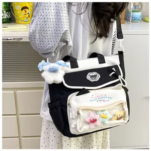 Detailed view of black and white canvas shoulder bag with transparent front pocket and charms.