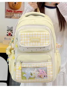 Detailed view of light yellow plaid student backpack with transparent ita window and charms.