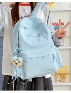 Light blue student backpack with cute bear pendant and embroidery details for daily travel.