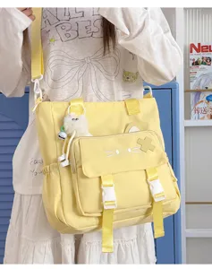Close up view of yellow canvas messenger bag with cute cat ears and fluffy pendant detail.