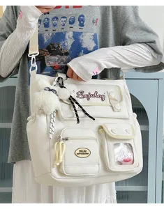 Detail view of the white canvas shoulder bag with multi-pockets, plush charm and clear pocket.