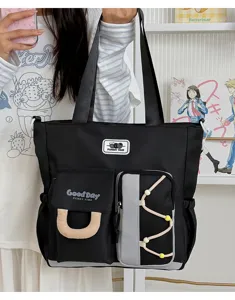Vista detallada del gran bolso tote negro de lona con múltiples bolsillos y correas.