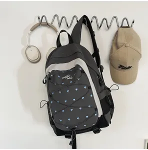 Close-up lifestyle detail of grey heart-print backpack with bungee cords and side mesh pockets.