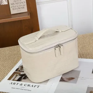 Vista detallada del bolso cosmético de cuero cocodrilo beige con doble cremallera.