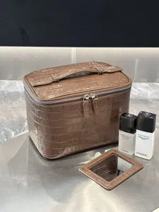 Vista detallada del bolso cosmetico marron de cuero genuino con patron de cocodrilo y cremallera.