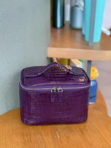 Detalle del bolso cosmético de cuero con textura de cocodrilo morado, cierre y asa.