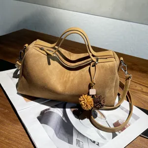Détail de sac Boston en daim marron, cuir souple, quincaillerie métallique et charmant pompon.