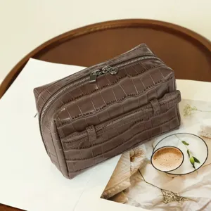 Close-up detail of crocodile textured cosmetic bag with smooth double metal zippers.