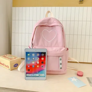 Detail shot of pink canvas backpack with white heart embroidery, front pocket on wooden desk.
