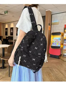 Detailed view of black quilted backpack with cute white bows, stylish casual student daypack.