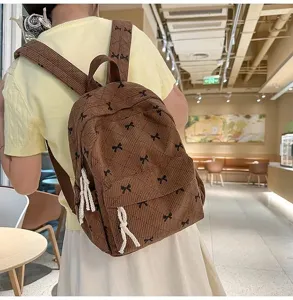 Detailed view of brown corduroy backpack with cute black bow prints and soft texture.