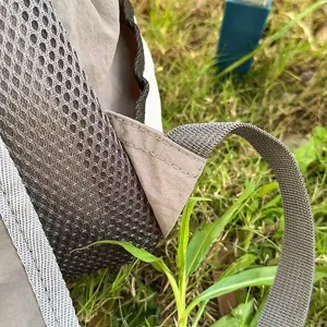 Close-up detail view of casual backpack shoulder strap and mesh pocket on green grass.