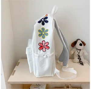 White backpack side detail featuring colorful embroidered flower patches and mesh shoulder straps.