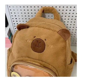 Primo piano del simpatico zaino in peluche marrone con viso ricamato e tasca frontale trasparente.
