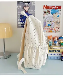 Detail view of a beige polka dot backpack on a tidy pastel desk, showing side pocket design.