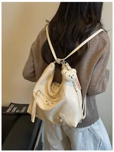 Close-up of women beige PU leather motorcycle backpack with metal studs and cute bear pendant.