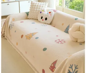 Close-up detail of beige fleece sofa blanket with cute cartoon Christmas tree and snowflake patterns.