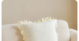 Detailaufnahme eines cremefarbenen Waffelmuster-Zierkissens mit feinen Rüschen auf Sofa.
