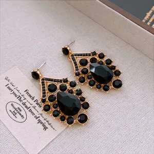 Primer plano de pendientes geométricos vintage dorados con cristal negro brillante.