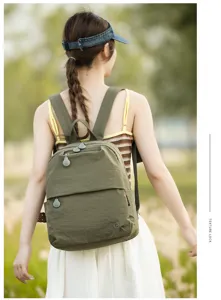 Outdoor detail view of a casual green nylon backpack worn by a model, featuring zipper design.