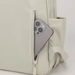 Detail shot of a light gray nylon backpack zipper pocket with phone insert and pull tab.