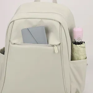 Close-up detail of the beige nylon backpack featuring front zip pocket and side slot.