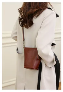 Detail shot of a chic brown leather bucket crossbody bag worn by a model from the back view.