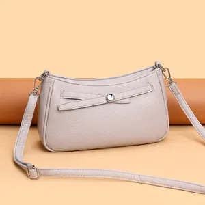 Detail view of stylish beige leather crossbody bag with chic metal button and adjustable strap.