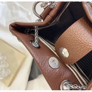 Close-up detail of brown litchi grain bucket bag with metal chain straps and rivets inside lining.