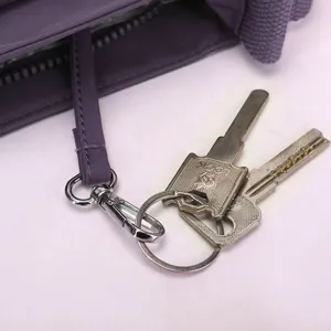 Detailed view of purple nylon crossbody bag interior keychain strap and metal hardware clip.
