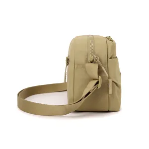 Close-up view of the khaki canvas crossbody bag side, showing zipper details and brand label.